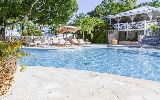 Travel X Exterior view of a serene pool area with lounge chairs, umbrellas, and a landscaped garden, adjacent to a building with a staircase and tropical foliage. Book your trip with Travel X and immerse yourself in this vacation paradise. Book Your Trip With Travel X