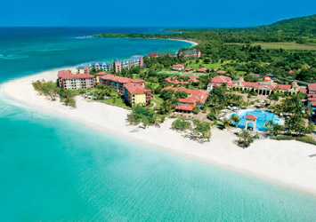 Travel X Aerial view of Travel X's beachfront resort with multiple buildings, a pool, and surrounding greenery against a backdrop of the ocean – the perfect vacation destination. Book Your Trip With Travel X