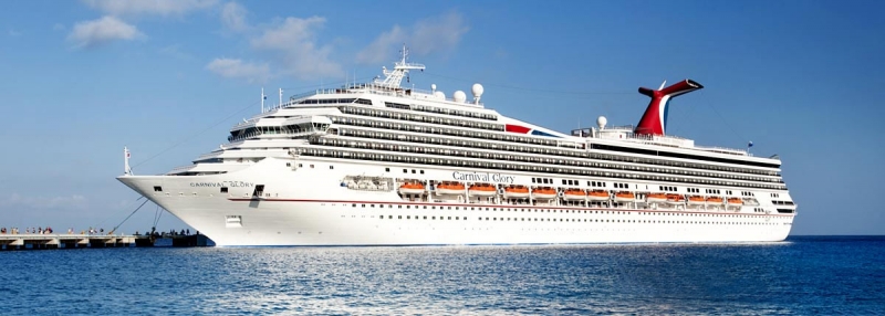 Travel X A large white cruise ship, resembling a floating resort, docked at a pier on a sunny day with blue skies and calm water. Book your trip with Travel X today! Book Your Trip With Travel X