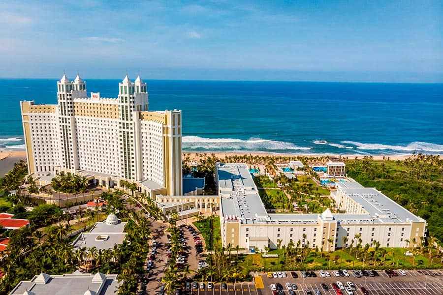 Travel X Aerial view of the Travel X beachfront resort complex with tall buildings, pools, and landscaped gardens near the ocean—ideal for your next vacation. Book Your Trip With Travel X