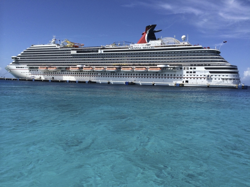 Travel X A large cruise ship named "Carnival Breeze" is docked in clear blue waters under a sunny sky, offering the perfect setting for a dream Vacation on Travel X's luxurious floating resort. Book Your Trip With Travel X