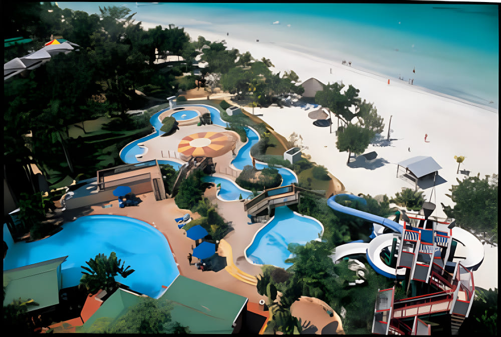 Travel X Aerial view of a beachfront resort featuring multiple swimming pools, a winding water slide, sunbathing areas, and shaded seating, with a sandy beach and ocean in the background. Book Your Trip with Travel X for the ultimate vacation experience. Book Your Trip With Travel X