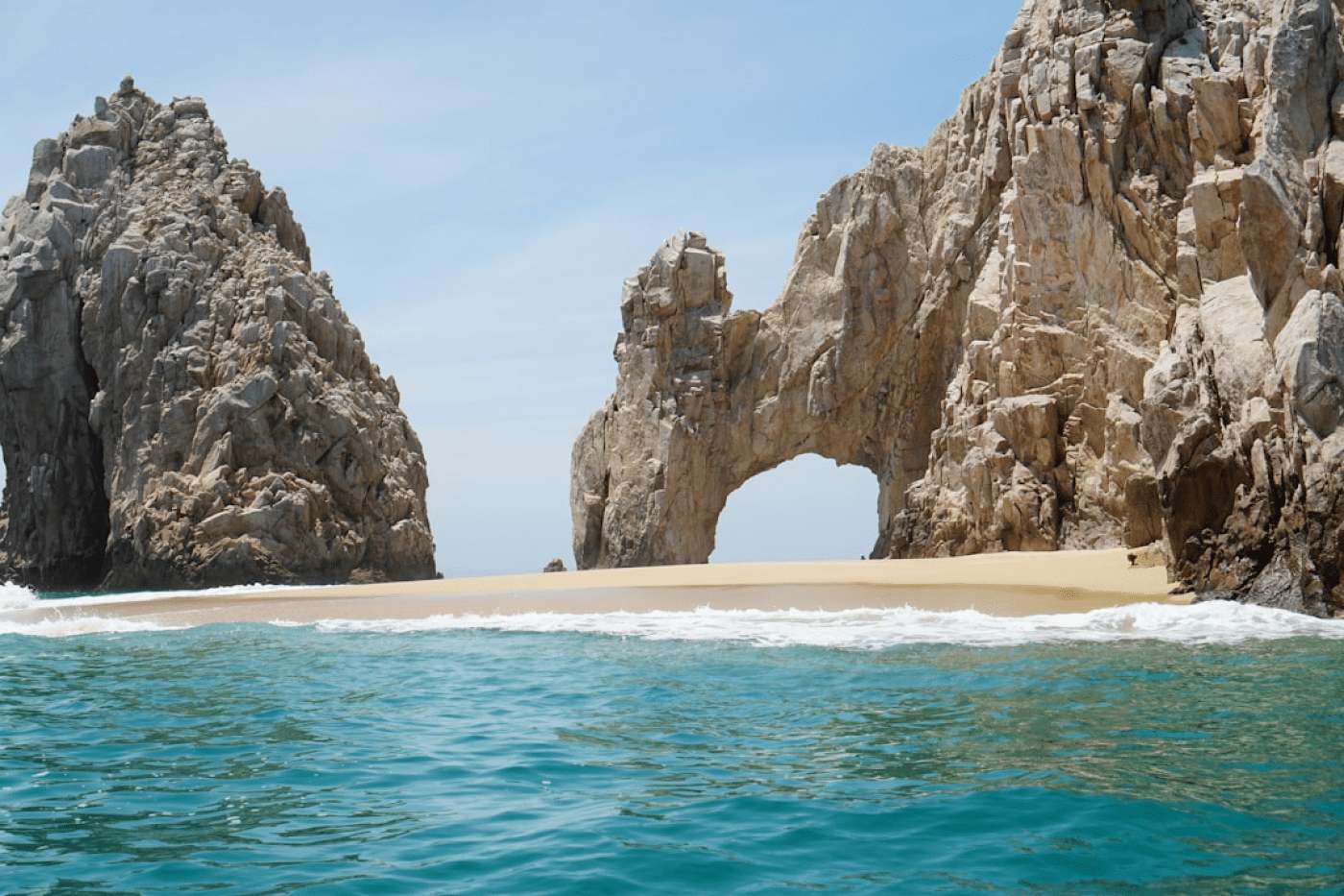 Travel X Rock formations with a natural arch and a sandy beach in a turquoise sea under a clear blue sky await you. Book your trip now to this stunning destination for the perfect vacation experience at our luxurious resort. Book Your Trip With Travel X