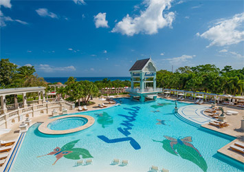 Travel X Large outdoor pool with "Sandals" written in blue on its bottom, tropical bird images, lounge chairs, a swim-up bar structure, palm trees, and clear blue skies in the background—your perfect resort vacation destination. Book Your Trip With Travel X