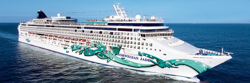 Travel X The Norwegian Jade, a large white cruise ship with teal decorative artwork on the hull, sails majestically in open water under a clear blue sky, promising the ultimate vacation experience. Book your trip now and enjoy our floating resort at sea. Book Your Trip With Travel X