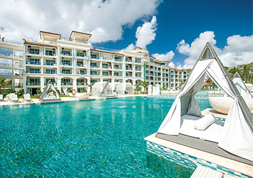 Travel X Experience the opulence of Travel X's luxurious resort, where white cabanas dot the edge of a large outdoor pool with clear blue water. White buildings with balconies grace the backdrop under a partly cloudy sky, creating the perfect setting for your dream vacation. Book Your Trip With Travel X