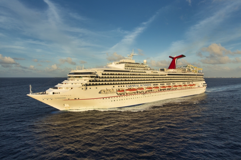 Travel X A large white cruise ship named Carnival Sunshine sails on a calm ocean under a blue sky with scattered clouds, offering a perfect vacation experience. Book Your Trip With Travel X