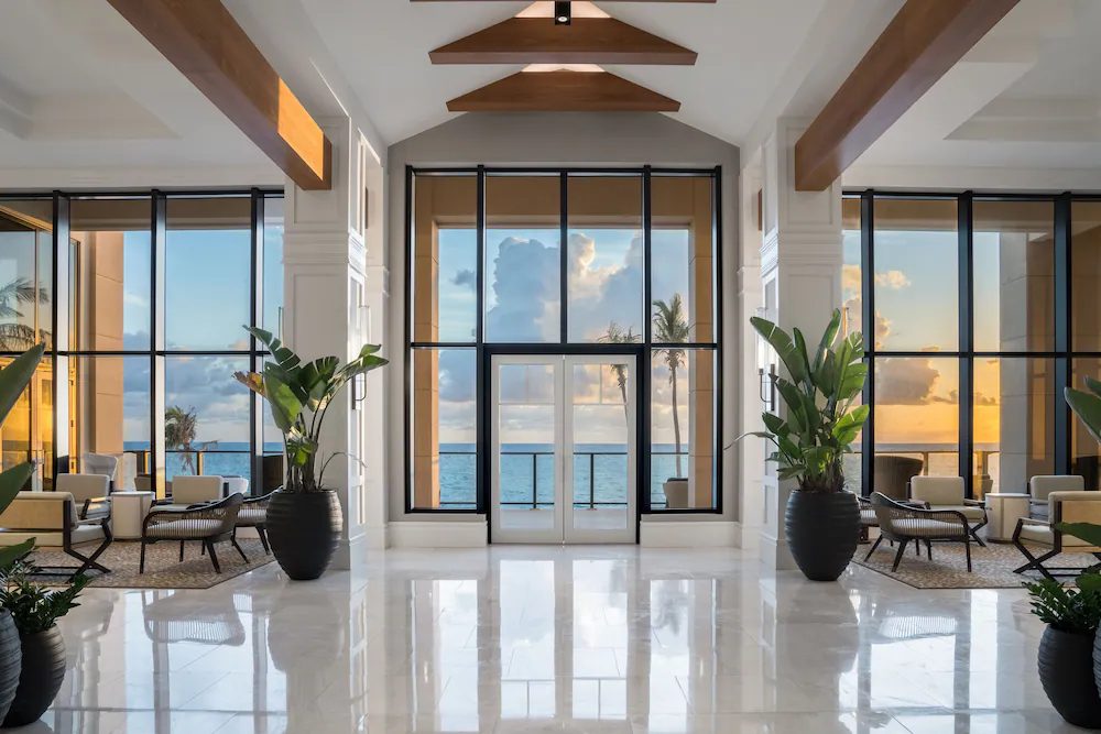 Travel X A bright, spacious lobby with large windows overlooking the ocean, indoor plants, and contemporary seating areas sets the perfect scene for your resort vacation. Book your trip and experience unparalleled relaxation. Book Your Trip With Travel X