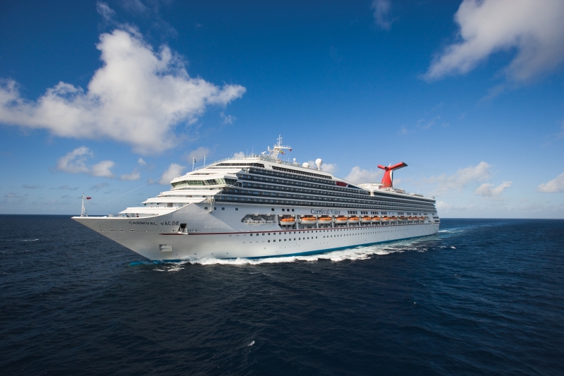 Travel X A white cruise ship with multiple decks and a red funnel sails in the ocean under a blue sky with scattered clouds, offering a perfect resort-like vacation. Book your trip now for an unforgettable experience. Book Your Trip With Travel X