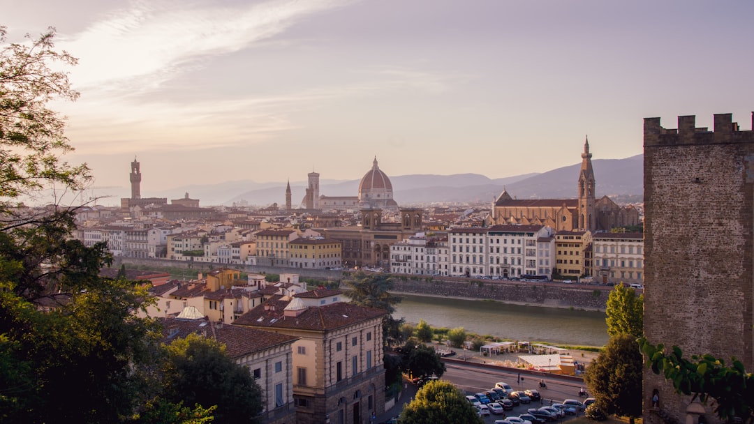 Travel X A panoramic view of Florence, Italy featuring the Arno River, the Florence Cathedral with its large dome, and surrounding historic buildings, with mountains in the background—an ideal Travel X vacation spot. Book Your Trip With Travel X