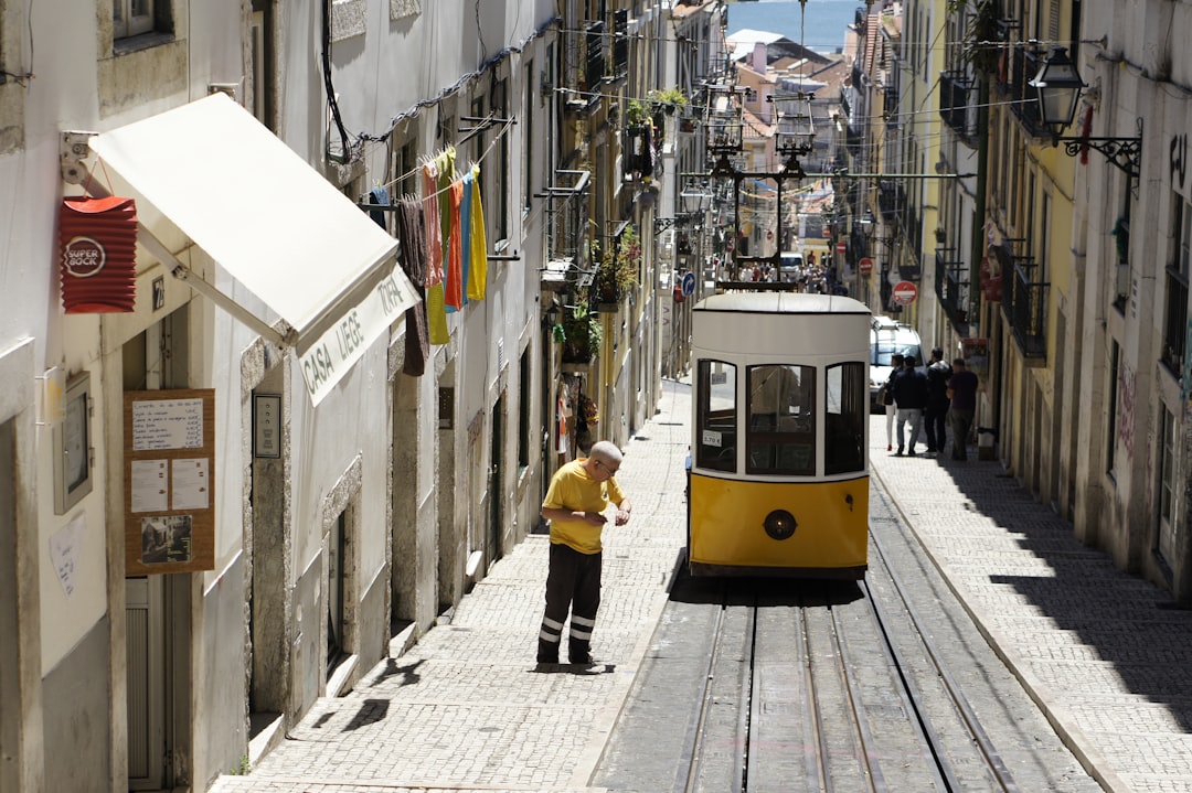 Travel X A yellow tram ascends a narrow, steep street lined with buildings, colorful laundry, and a few pedestrians—discover this charming destination with Travel X and book your trip today. Book Your Trip With Travel X