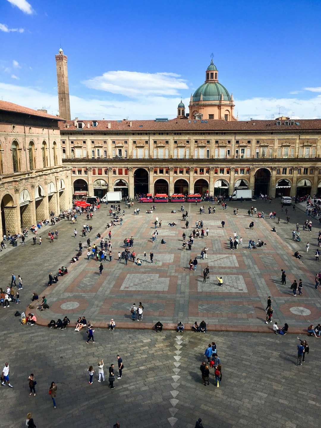 Travel X A large open square with patterned paving, dotted with people sitting and walking, surrounded by historic buildings and arches. A dome and tall tower are visible in the background under a blue sky. Perfect for your next Vacation, discover Travel X to book your trip today! Book Your Trip With Travel X