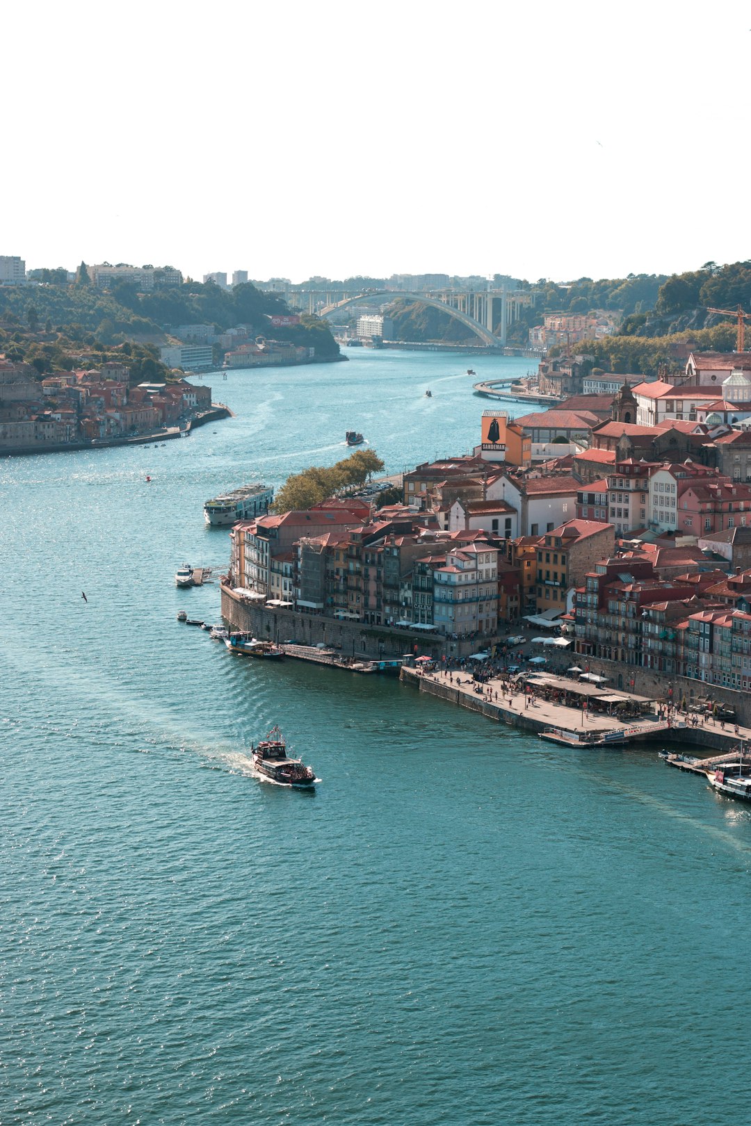 Travel X Aerial view of a river with boats and a hilly urban landscape featuring densely packed buildings along the waterfront makes for an ideal Travel X vacation. Book Your Trip With Travel X